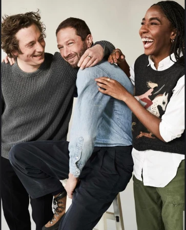 Three people smiling together in a studio shot. Two men and a woman are casually dressed, exuding a cheerful and friendly vibe.