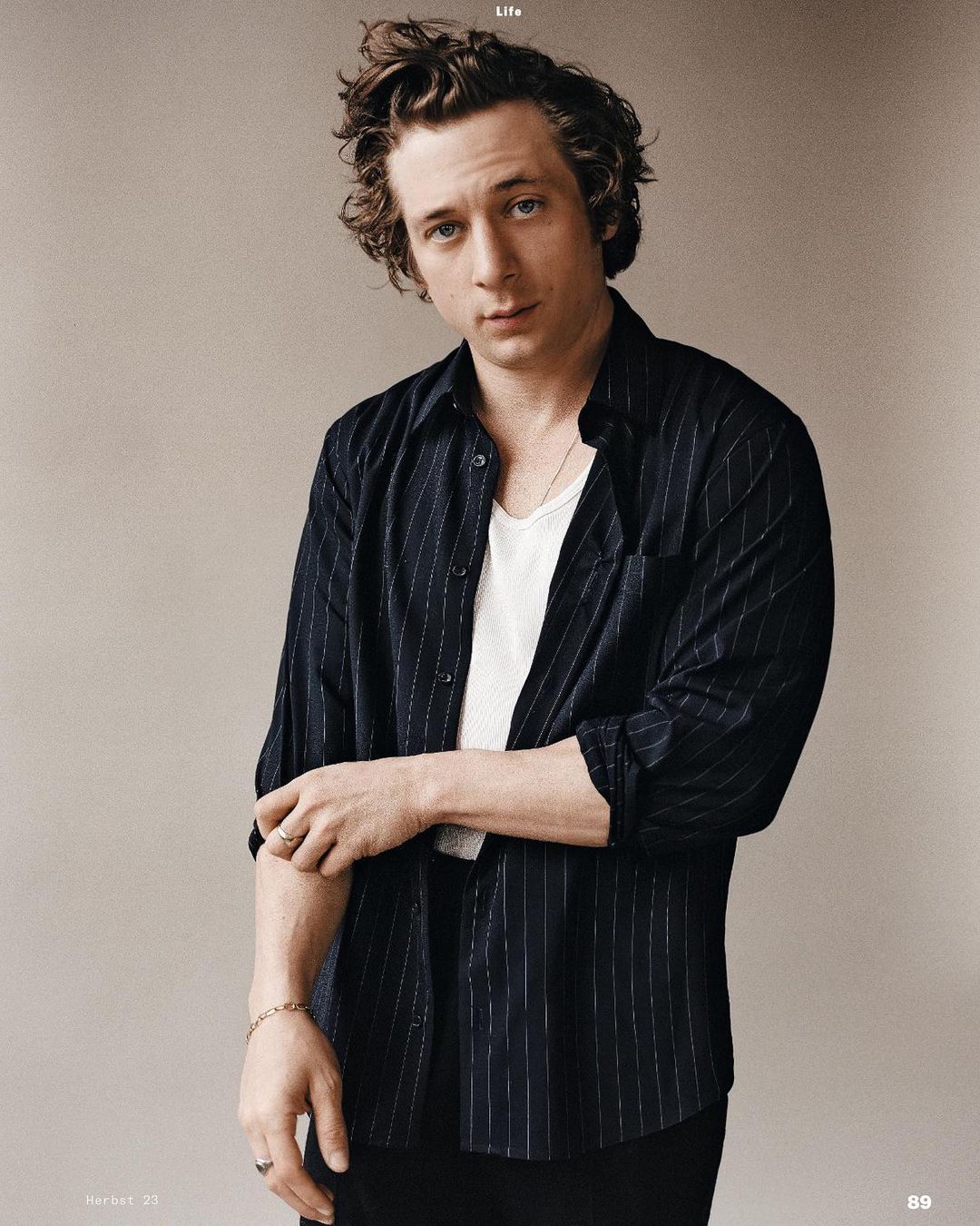 Portrait of Jeremy Allen White wearing a black and white striped shirt in a studio setting. He looks directly at the camera.