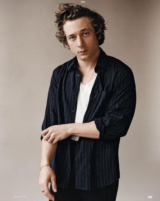 Portrait of Jeremy Allen White wearing a black and white striped shirt in a studio setting. He looks directly at the camera.