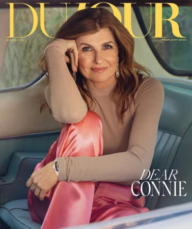 Connie Britton seated inside a vintage car wearing a beige ribbed top and shiny pink trousers, photographed by Victoria Stevens.