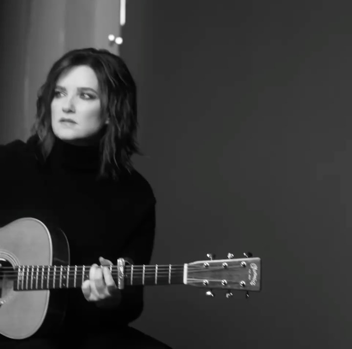 Monochrome portrait of a brunette adult female playing an acoustic guitar in a studio environment, showcasing musical artistry.