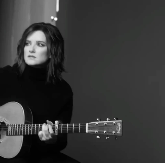 Monochrome portrait of a brunette adult female playing an acoustic guitar in a studio environment, showcasing musical artistry.