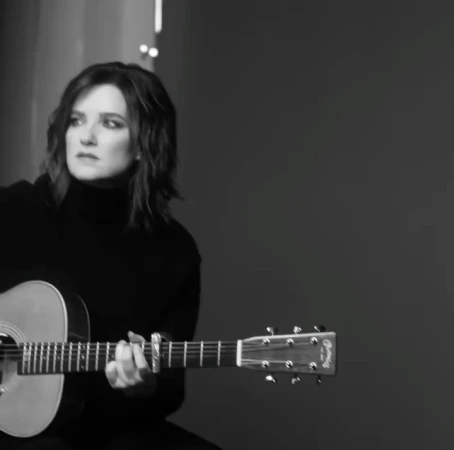 Monochrome portrait of a brunette adult female playing an acoustic guitar in a studio environment, showcasing musical artistry.