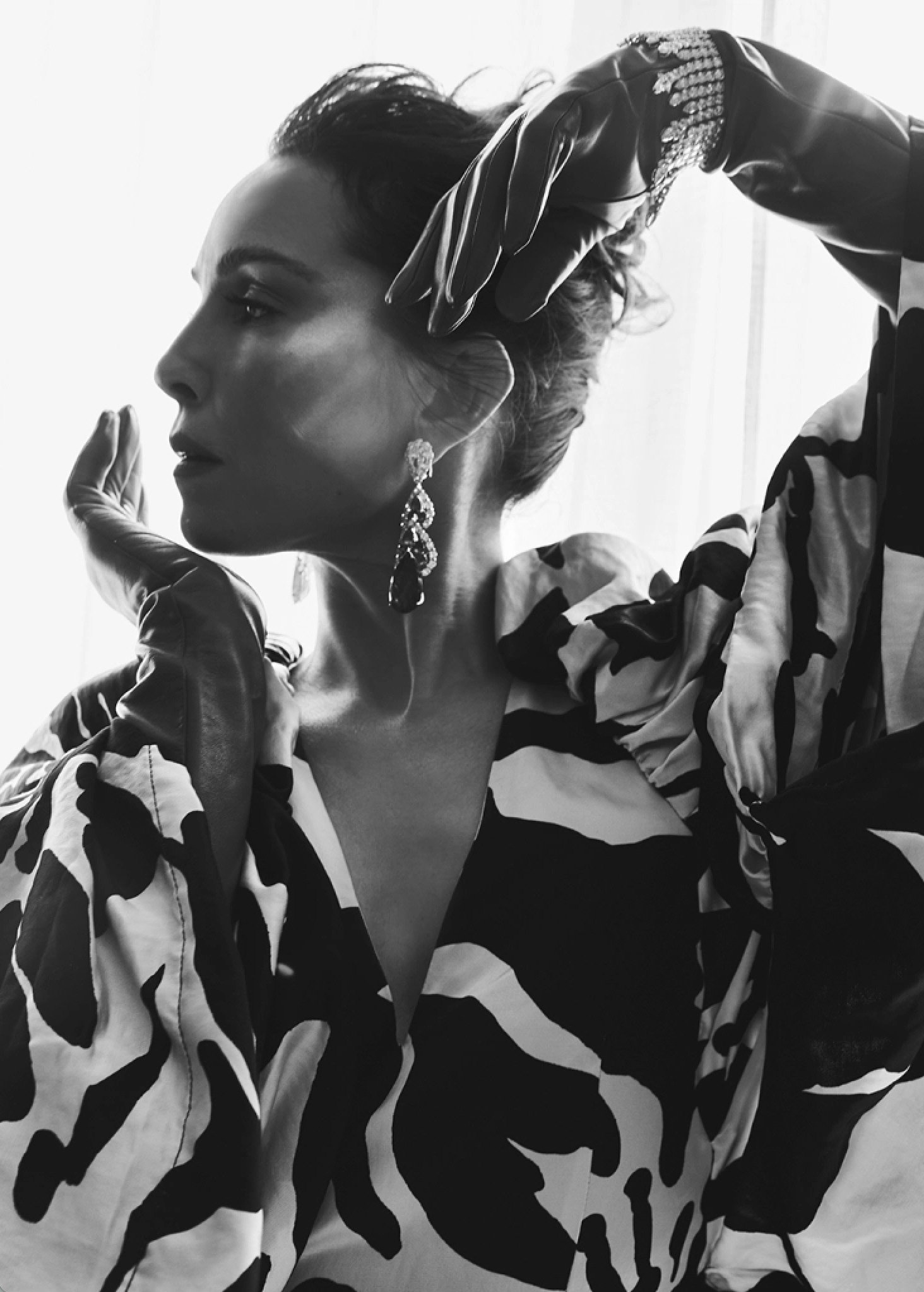 Monochrome portrait of a woman in profile wearing patterned garments, leather gloves, and large dangling earrings by Victoria Stevens.