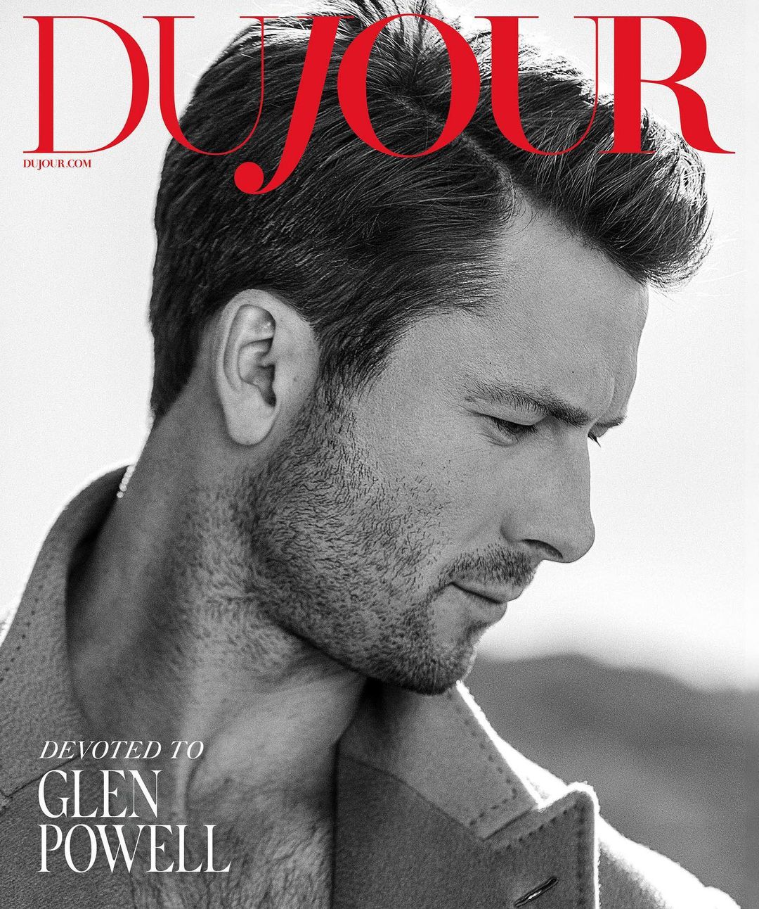 Black and white portrait of Glen Powell on a magazine cover. The magazine is 'DUJOUR' and the text says, 'Devoted to Glen Powell'.