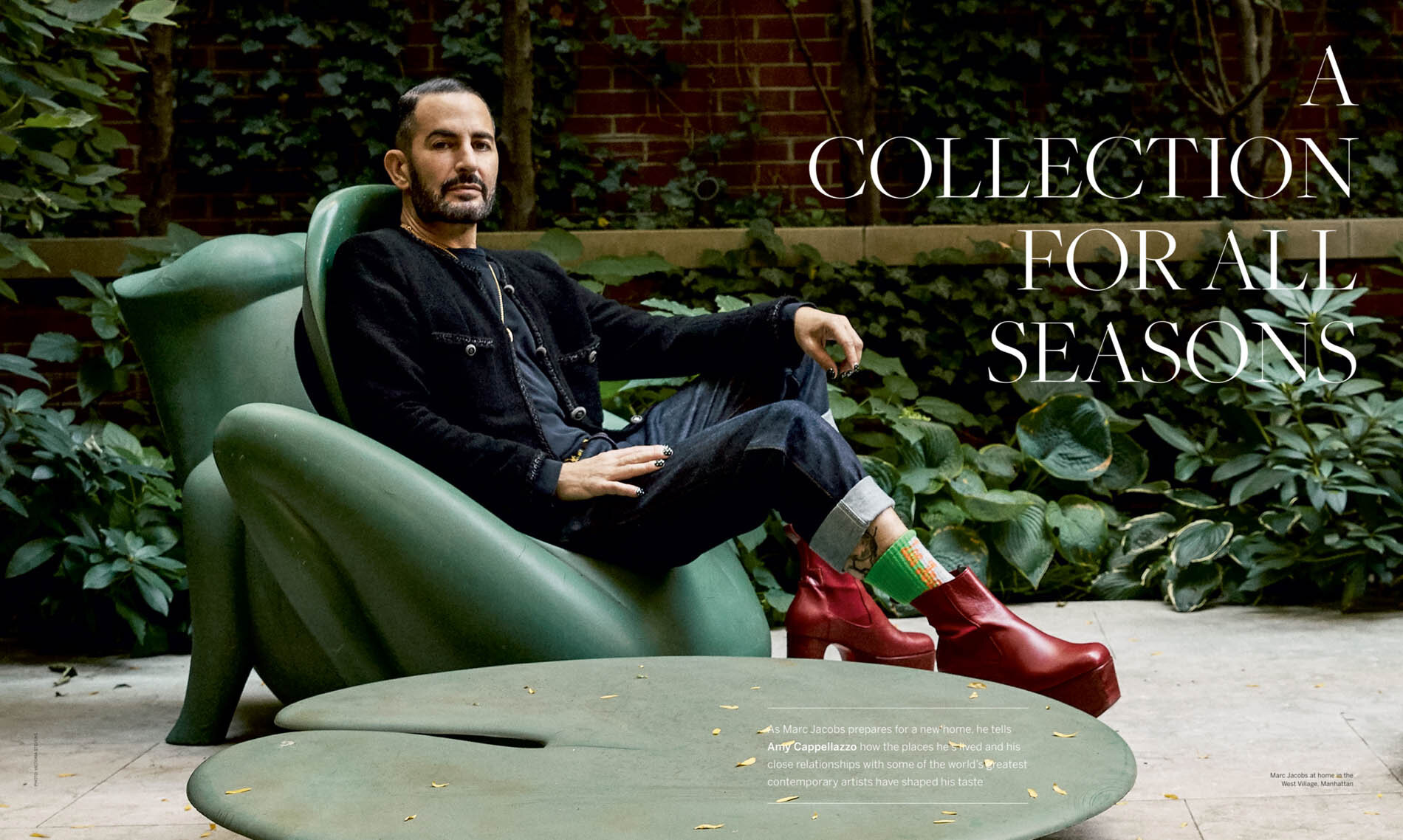 Marc Jacobs sitting in a large green frog-shaped chair, wearing a black jacket, dark jeans, and red platform boots, outdoors.