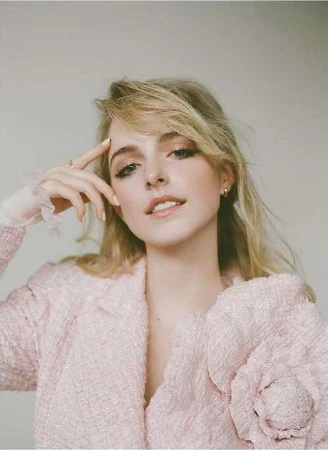 Portrait of a blonde woman with neutral makeup and a pink tweed jacket posing against a plain background in a studio setting.