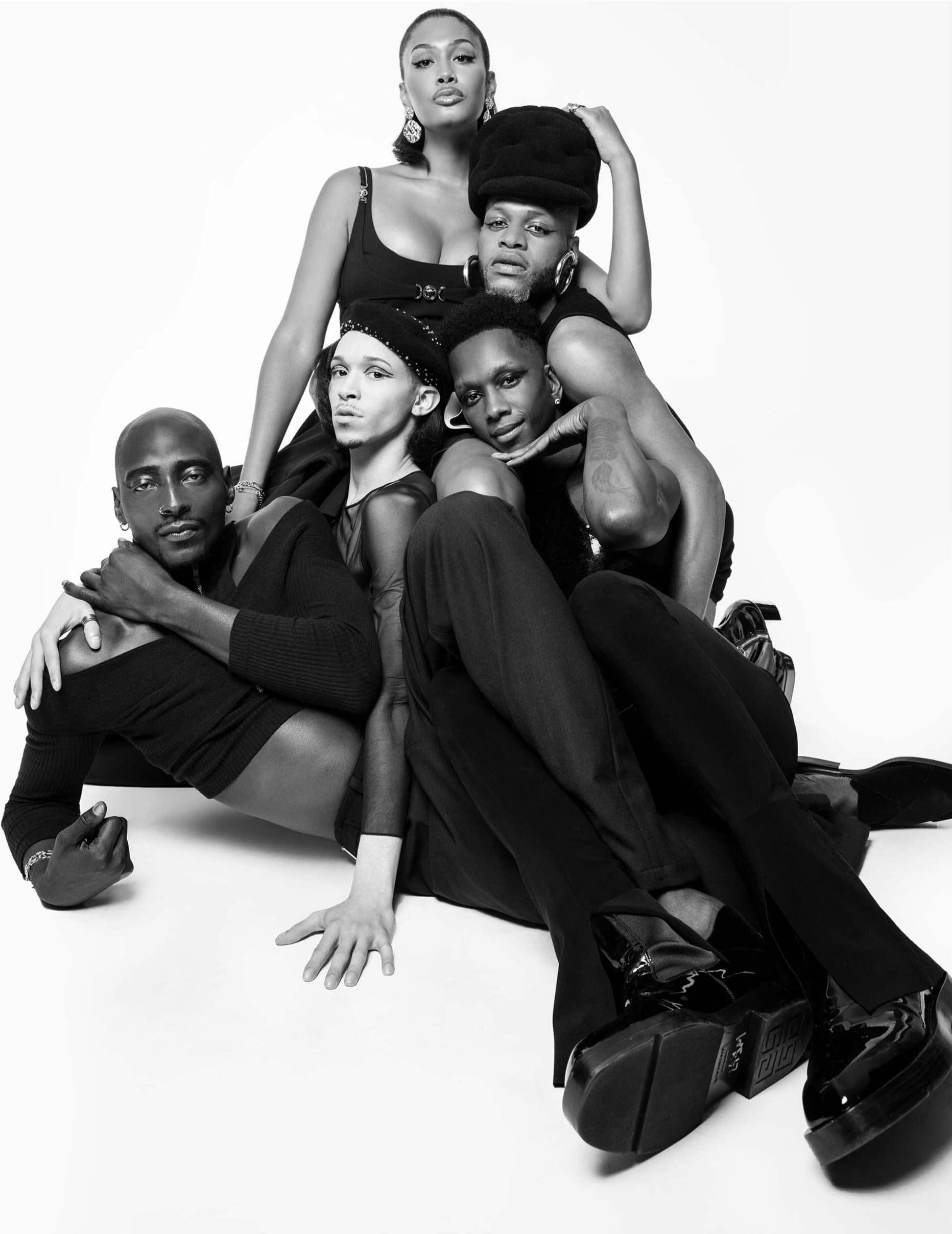 Black and white portrait of a group of five fashionably styled people posing in front of a white backdrop in a studio setting.