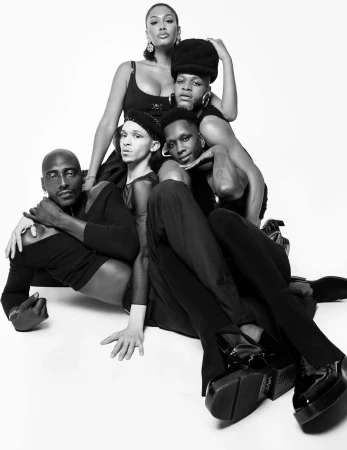Black and white portrait of a group of five fashionably styled people posing in front of a white backdrop in a studio setting.