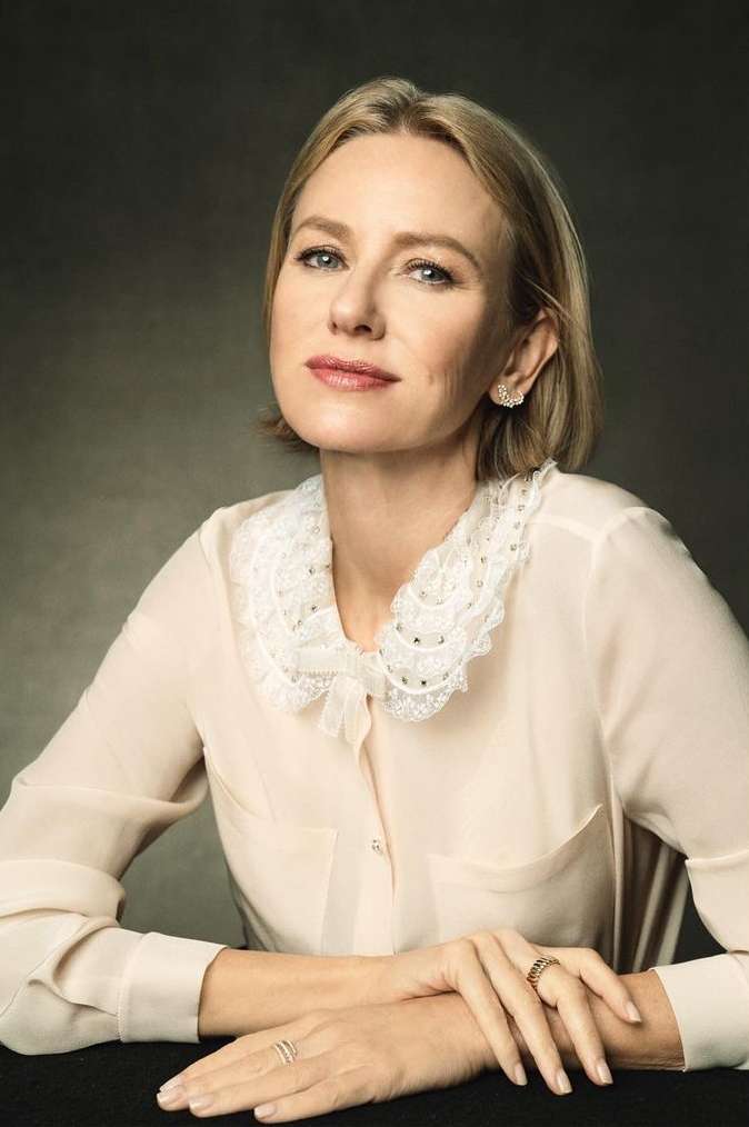 Close-up studio portrait of Naomi Watts, fair-skinned woman with blonde bob, wearing a cream-colored blouse with a lace collar.