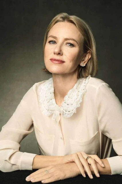 Close-up studio portrait of Naomi Watts, fair-skinned woman with blonde bob, wearing a cream-colored blouse with a lace collar.