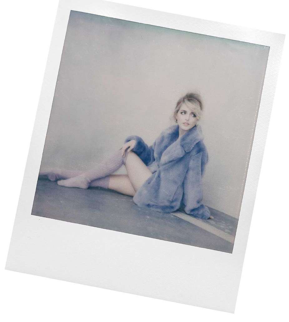 A woman poses in a lavender faux-fur coat and matching leg warmers in a Polaroid-style frame against a gray background.