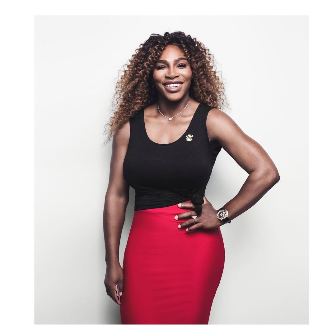 Portrait of smiling Serena Williams in a black top and red skirt against a white backdrop, showcasing her elegant and athletic physique.