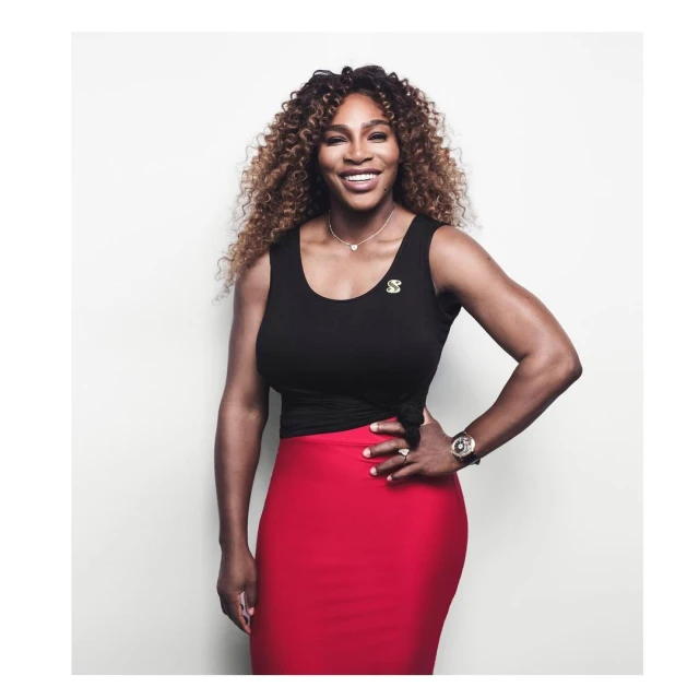 Portrait of smiling Serena Williams in a black top and red skirt against a white backdrop, showcasing her elegant and athletic physique.