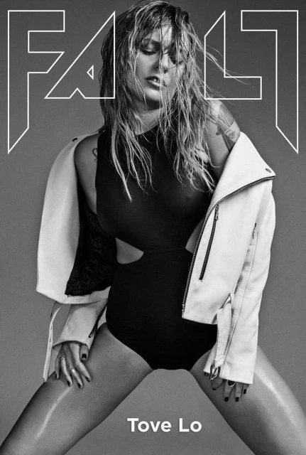 Black and white portrait of blonde woman wearing black bodysuit and white jacket for magazine cover, shot in a photo studio.