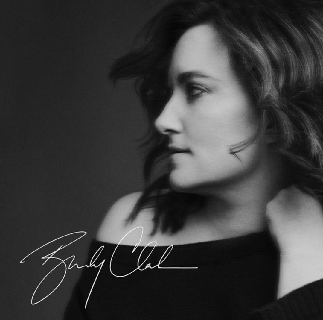 Black and white profile portrait of a woman with dark hair wearing an off-the-shoulder dark top, photographed by Victoria Stevens.
