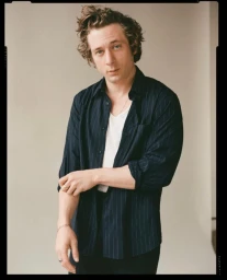 Jeremy Allen White wearing a dark pinstripe shirt and white t-shirt against a neutral studio background.