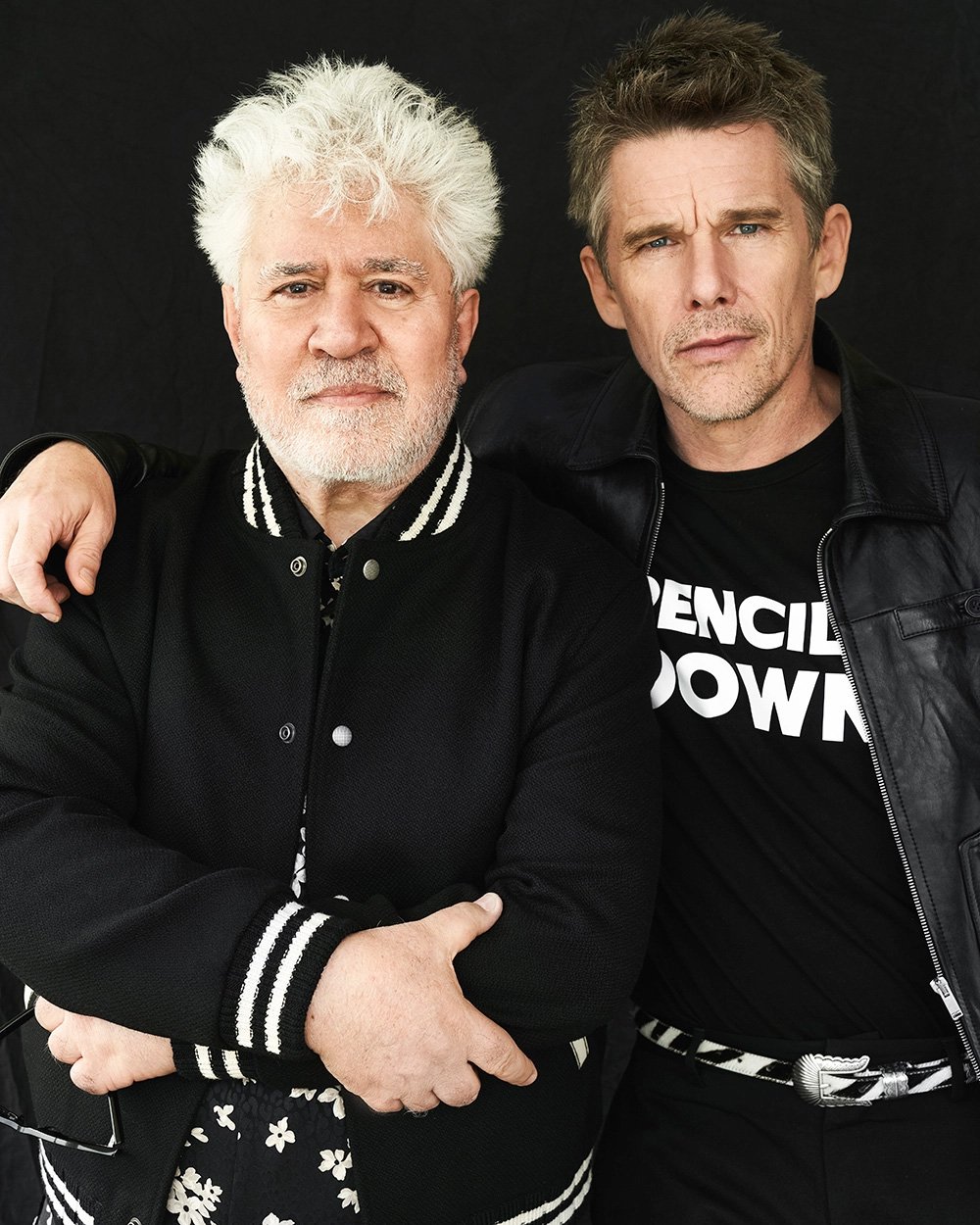 Portrait of Pedro Almodovar and Ethan Hawke standing together against a plain dark background, photographed by Victoria Stevens.