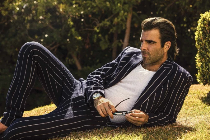 Man wearing a navy blue pinstripe suit and white t-shirt lying on a grassy lawn outdoors.