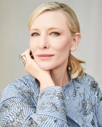 Close-up portrait of Cate Blanchett wearing a blue and white striped shirt with beaded embellishments, resting chin on hand.