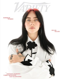 Portrait of Billie Eilish with dark hair and red highlights wearing a white button-down shirt with black floral applique against a white background.