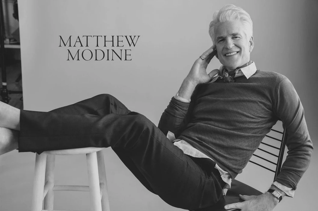 Portrait of actor Matthew Modine smiling with feet propped up on a stool, photographed by Victoria Stevens.