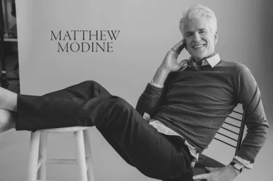 Portrait of actor Matthew Modine smiling with feet propped up on a stool, photographed by Victoria Stevens.