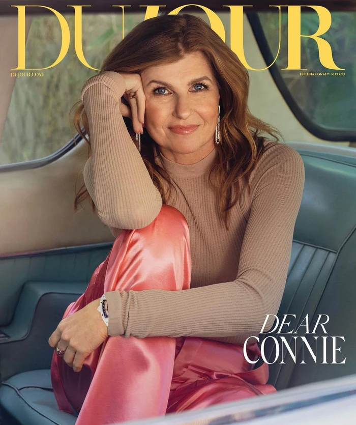 Connie Britton seated inside a vintage car wearing a beige ribbed top and shiny pink trousers, photographed by Victoria Stevens.