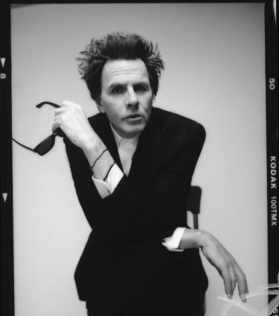 Portrait of a man in a dark suit holding sunglasses against a white background by photographer Jonny Marlow.