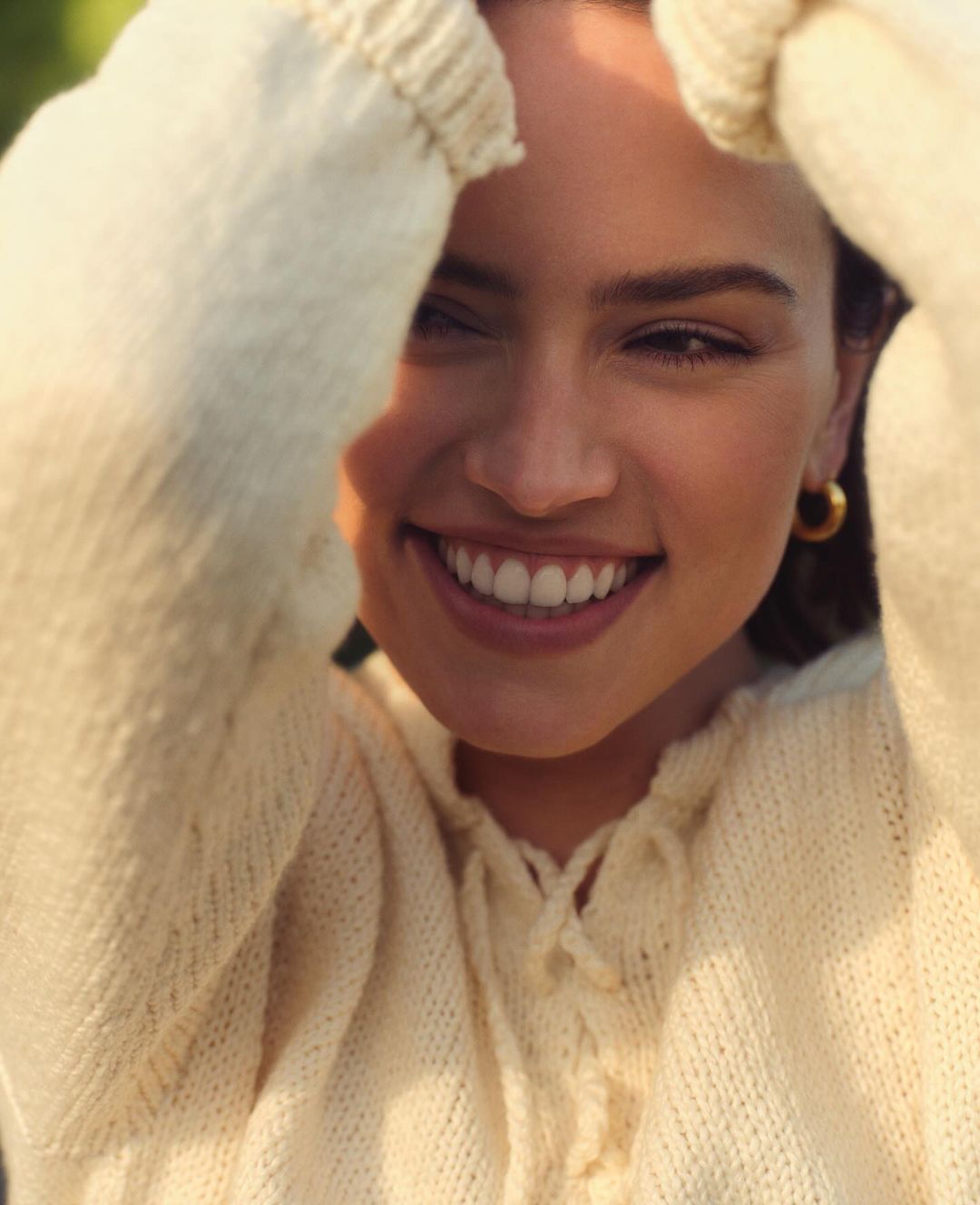 Portrait of a smiling adult female wearing a white sweater. Close-up shot highlighting facial features and soft, natural outdoor lighting.