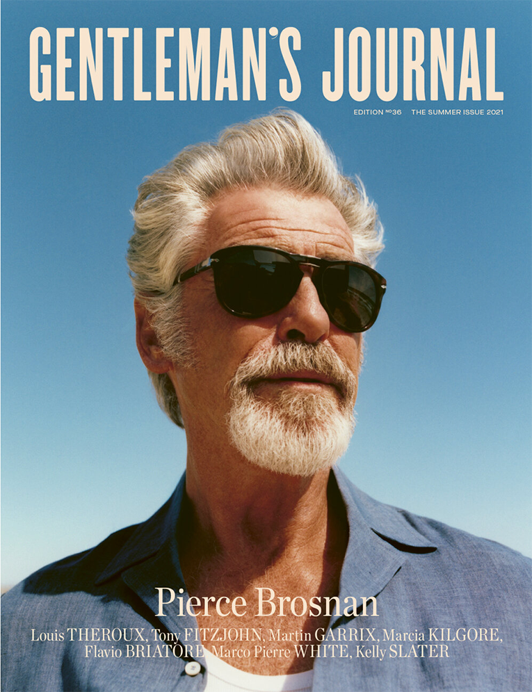 Gentleman's Journal magazine cover featuring Pierce Brosnan wearing sunglasses and a blue shirt against a clear blue sky background.