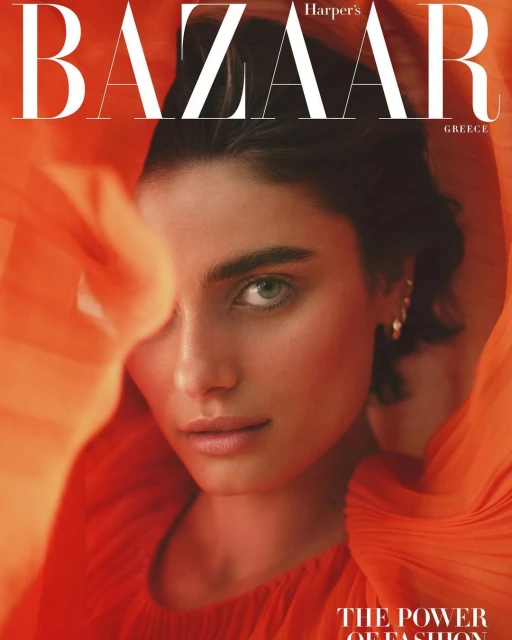 Close-up portrait of a woman with fair skin and green eyes, wearing a red top, against an orange background. Harper's Bazaar magazine cover.