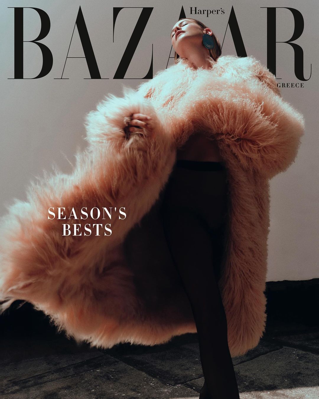 Harper's Bazaar Greece cover featuring a woman in a voluminous faux fur coat, set against a studio backdrop with visible magazine text.