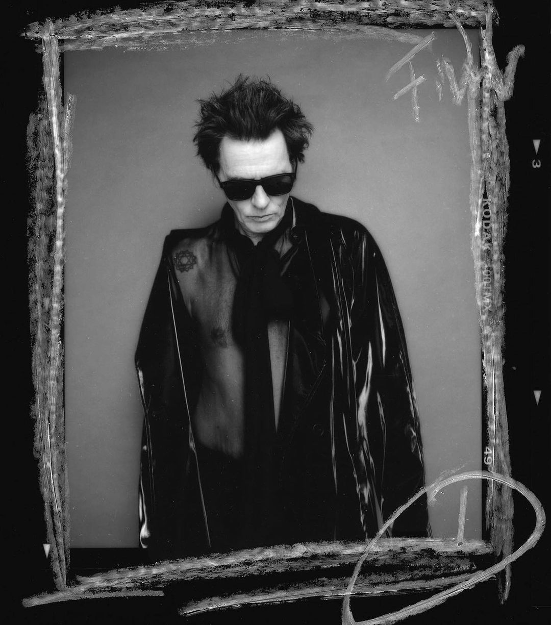 Monochrome portrait of a man with dark hair, sunglasses, and a sheer jacket against a neutral background in a chalk-drawn frame.