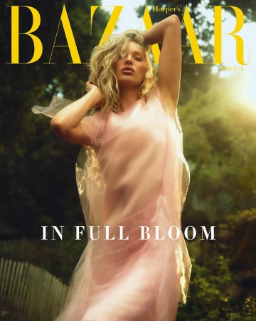 Blonde woman wearing a sheer pink dress posing outdoors in sunlight with trees in the background