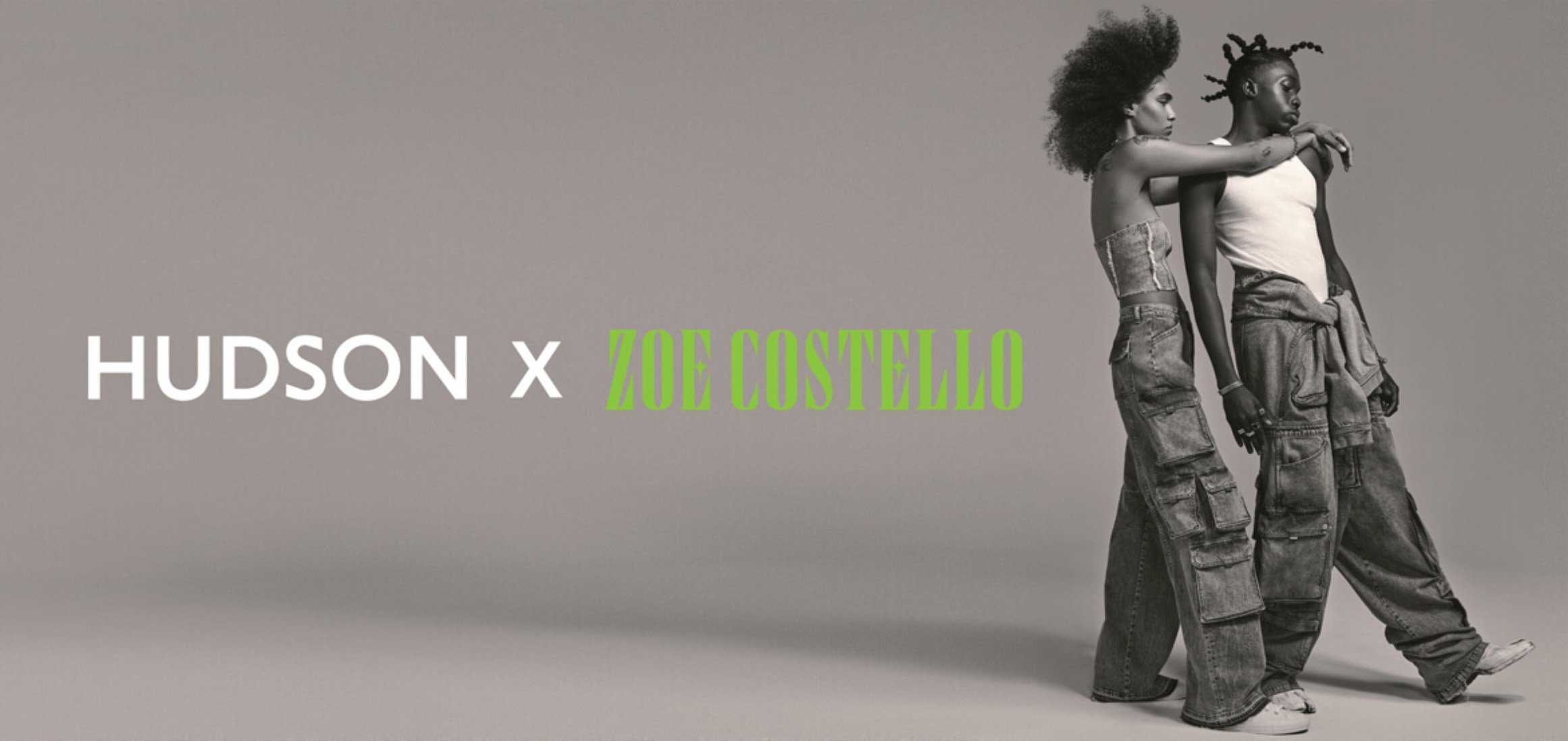 Fashion shot of a couple wearing matching denim cargo pants in front of a grey backdrop with the HUDSON x ZOE COSTELLO logo.