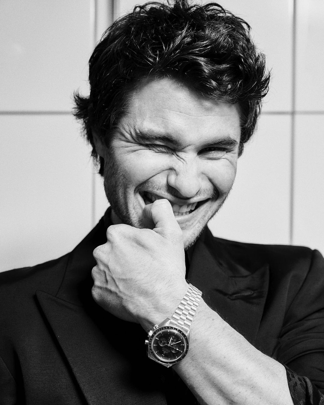 Portrait of Ansel Elgort laughing and biting his thumb while wearing a blazer and a metal watch by photographer Jonny Marlow.