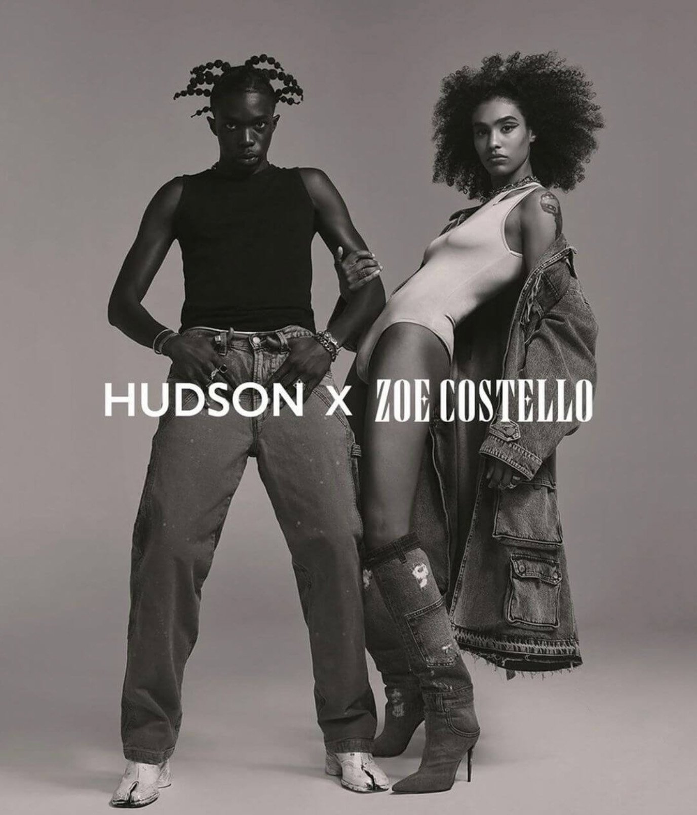 Two models, an adult male and an adult female, pose in an indoor studio setting. The image has a black and white color scheme.
