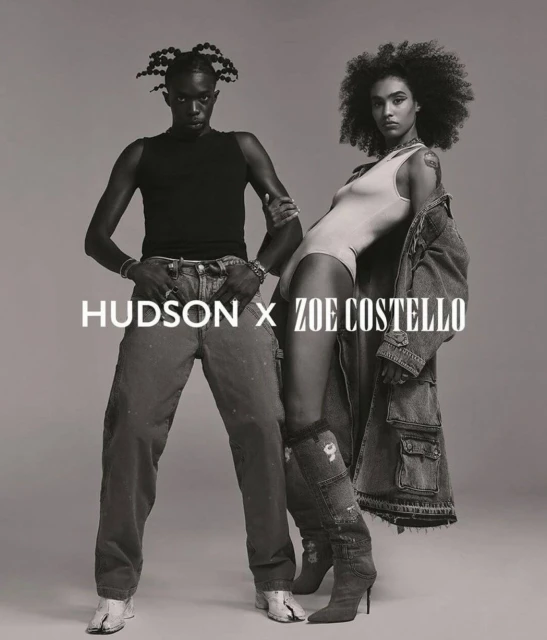 Two models, an adult male and an adult female, pose in an indoor studio setting. The image has a black and white color scheme.