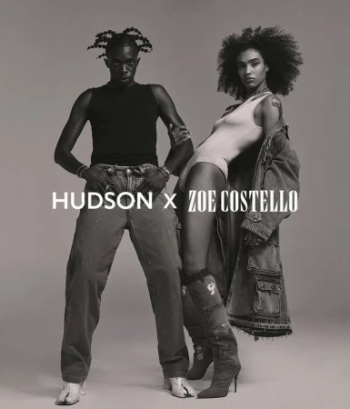 Two models, an adult male and an adult female, pose in an indoor studio setting. The image has a black and white color scheme.