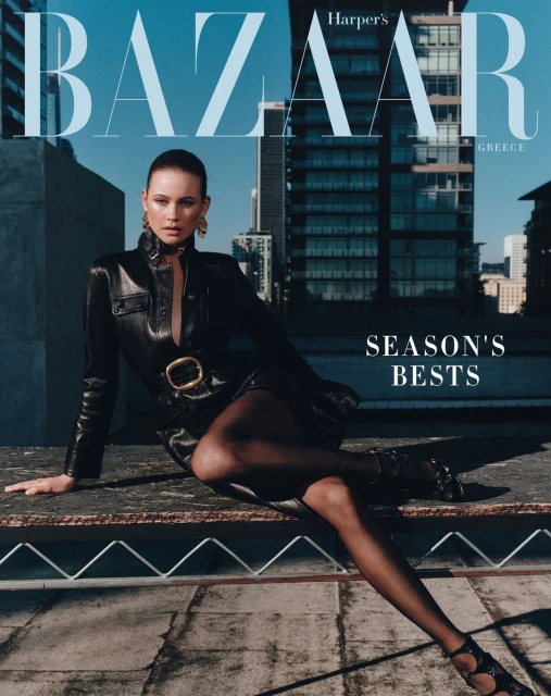 Fashion magazine cover with a woman in a black leather dress and hose sitting on a rooftop, with city buildings in the background.