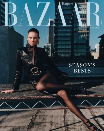 Fashion magazine cover with a woman in a black leather dress and hose sitting on a rooftop, with city buildings in the background.