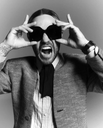 Monochrome portrait of a man holding up oversized dark sunglasses while shouting with an expressive face.