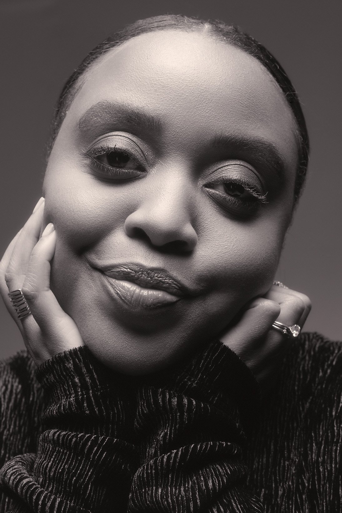 Close-up monochrome portrait of a black woman smiling with hands on cheeks