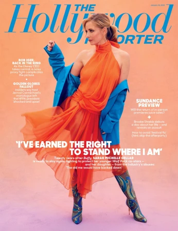 Magazine cover featuring Sarah Michelle Gellar wearing an orange dress, boots, and blue coat against a peach background, in a studio shot.