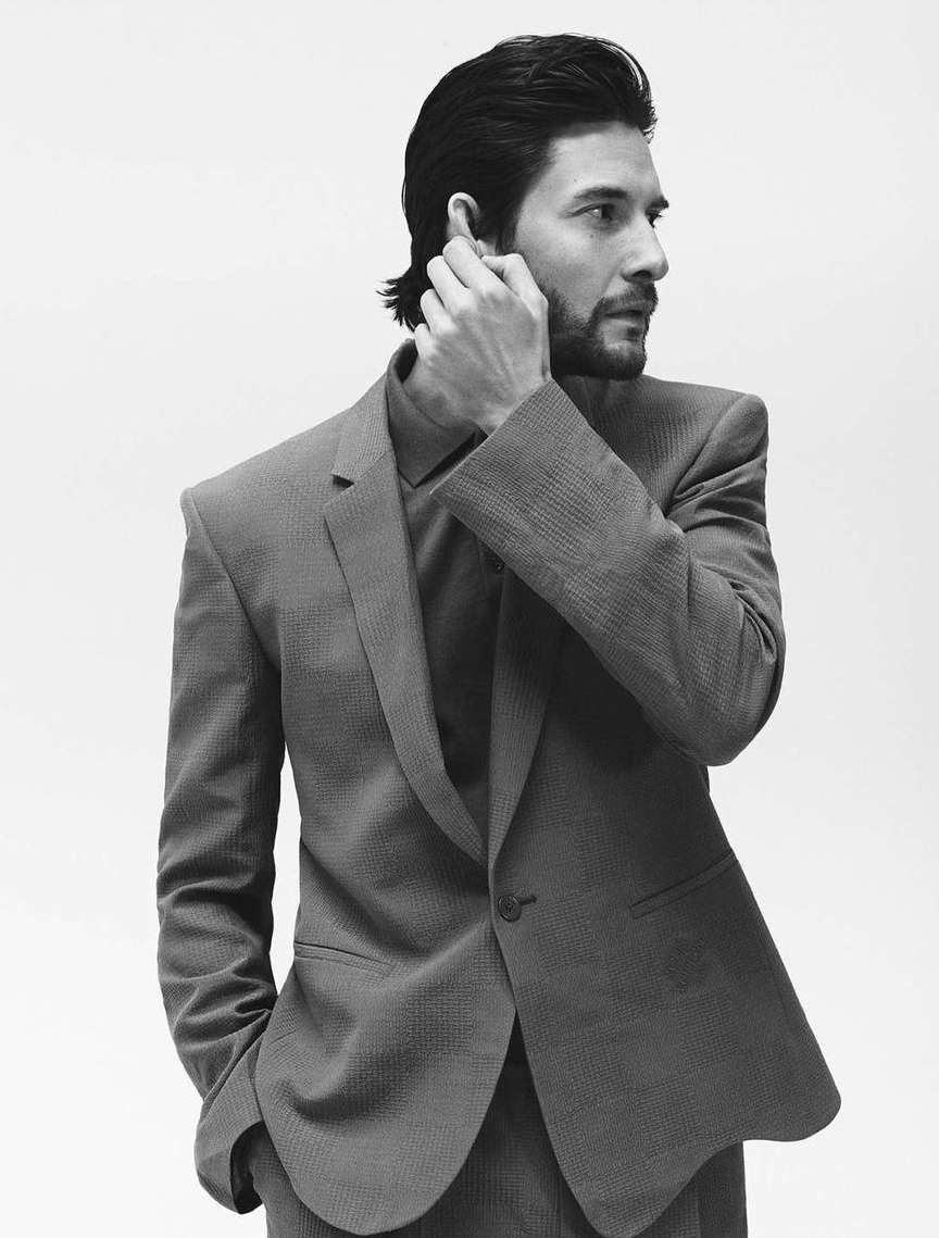 Monochrome portrait of Ben Barnes wearing a tailored suit, adjusting his hair against a plain white studio background.