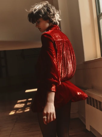 Model with short curly hair wearing a shiny red dress standing near a window in Los Angeles captured by Jonny Marlow.
