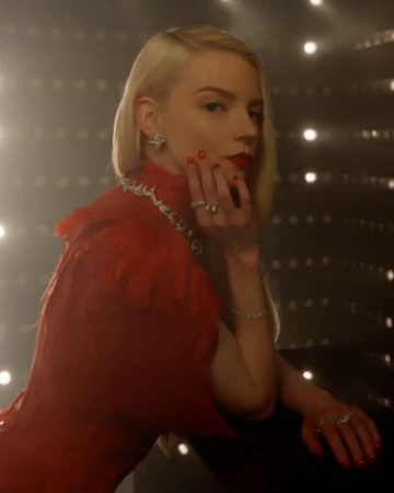 Anya Taylor-Joy wearing a red dress with sparkling jewelry against a warm dark background with glowing lights, photographed by Sharif Hamza.