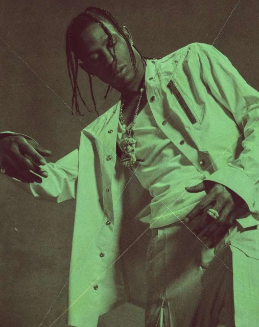 Male model poses in a white jacket and pants with jewelry against a dark background, highlighted with a green color grading effect.