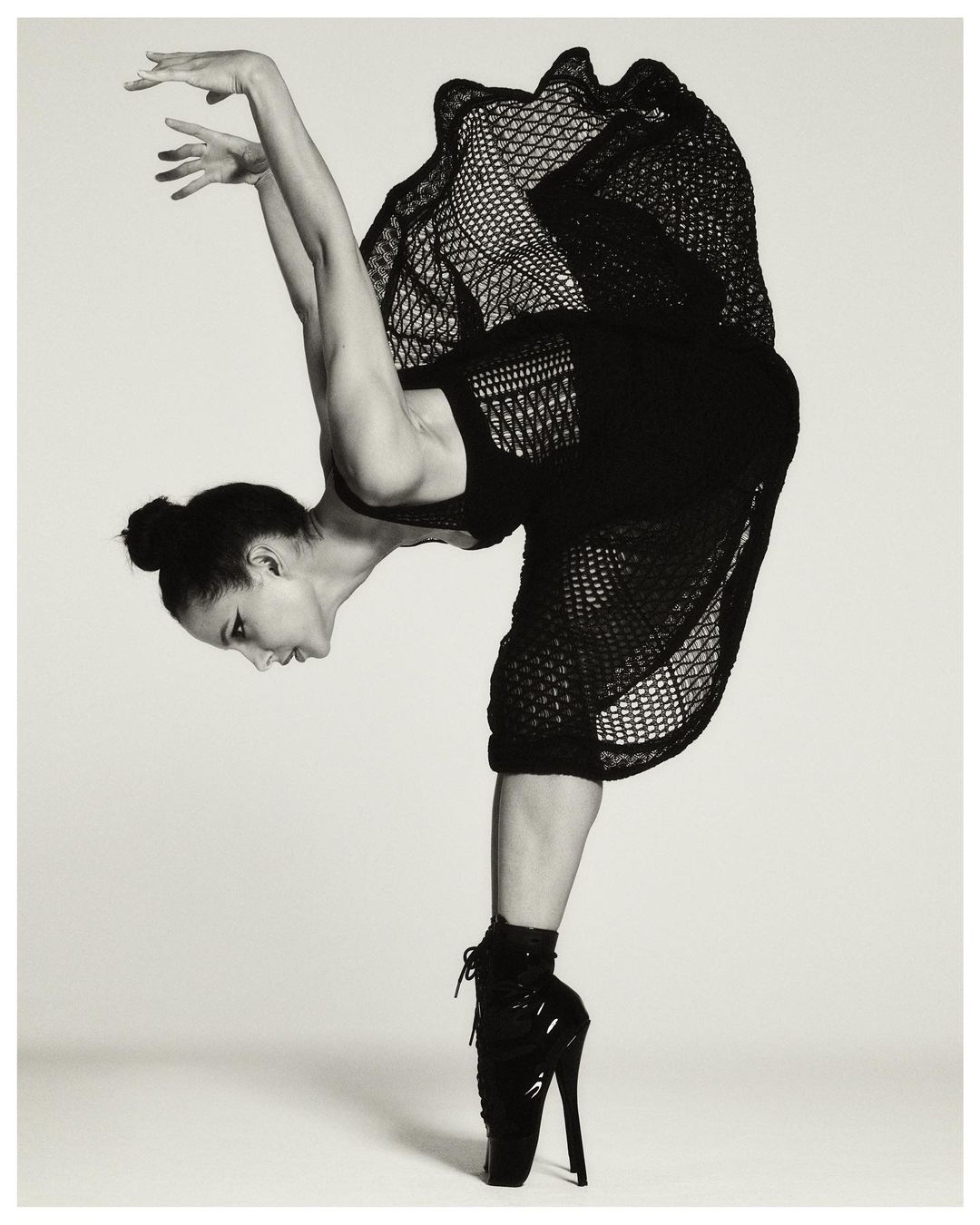 A ballet dancer balances en pointe in a black dress. The dancer strikes a dramatic pose against a light grey background.